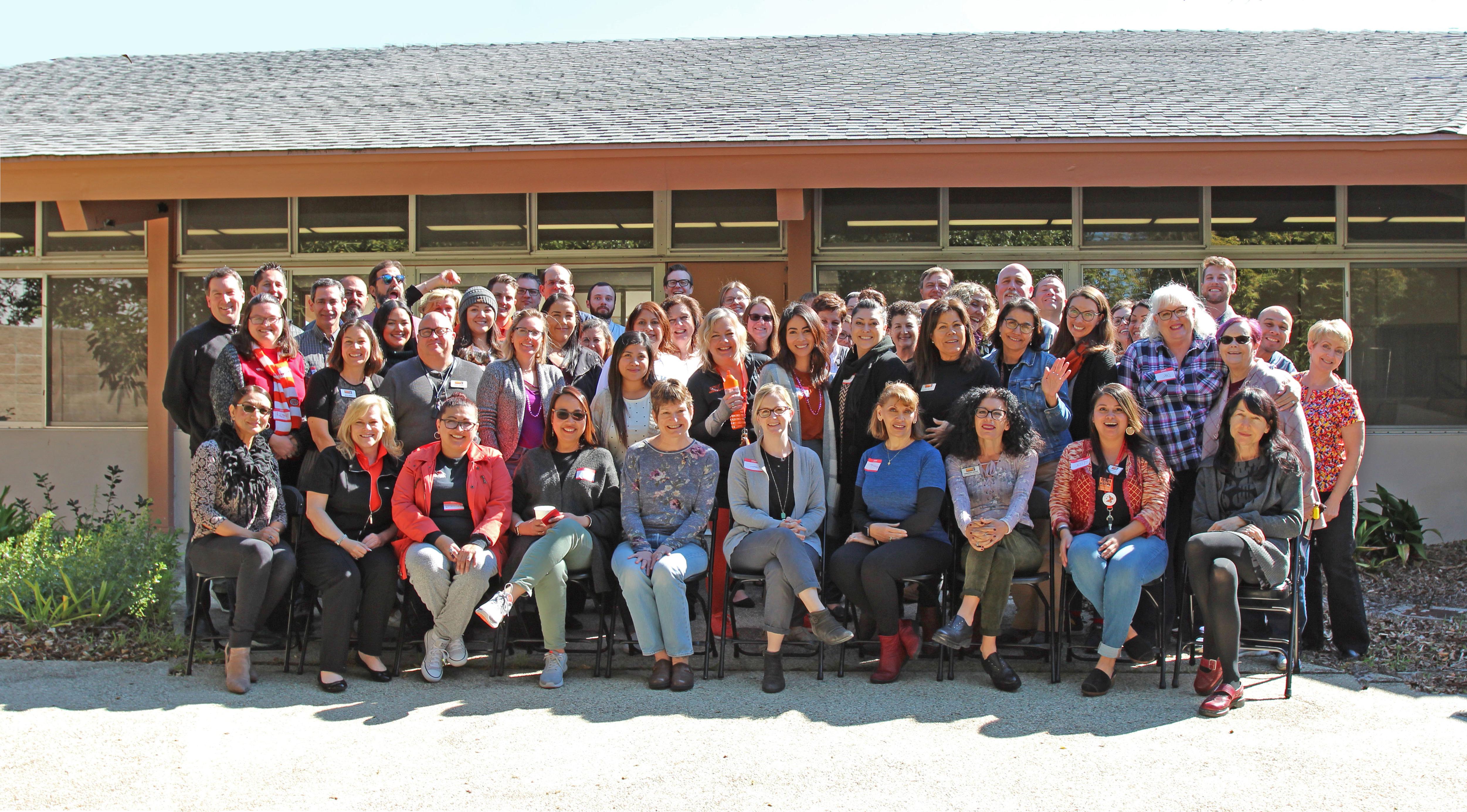 Group Photo of 澳门皇家赌城在线大学 staff at college wide even in the patio of Wright Event Center. The sun is shinning.